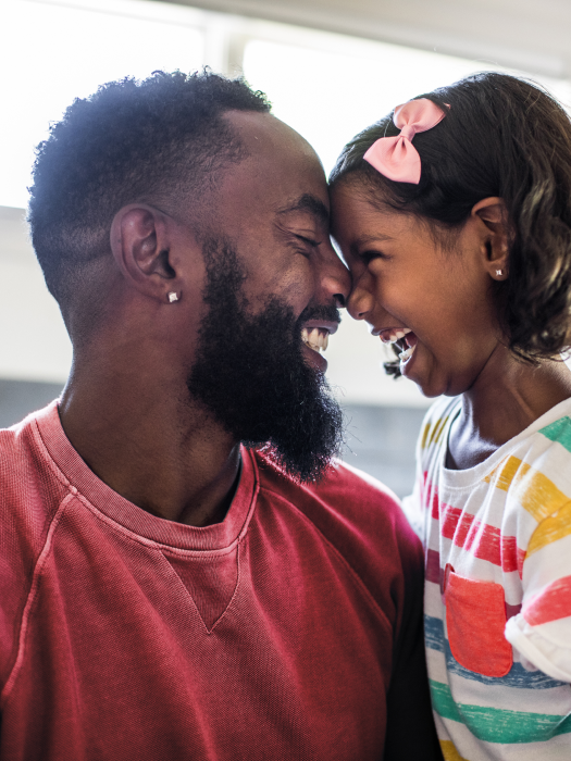 Black dad with curly hair smiling at his daughter with their noses touching