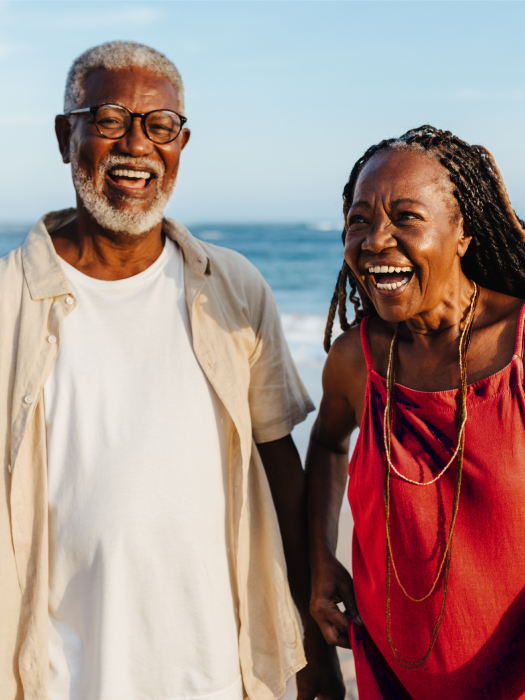 Active eldery black couple laughing walking along the beach