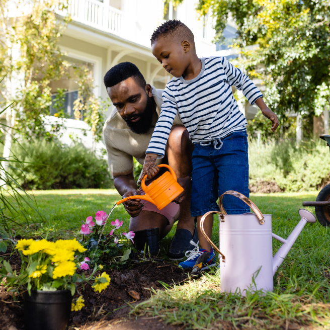 Father helps son pour water can in garden